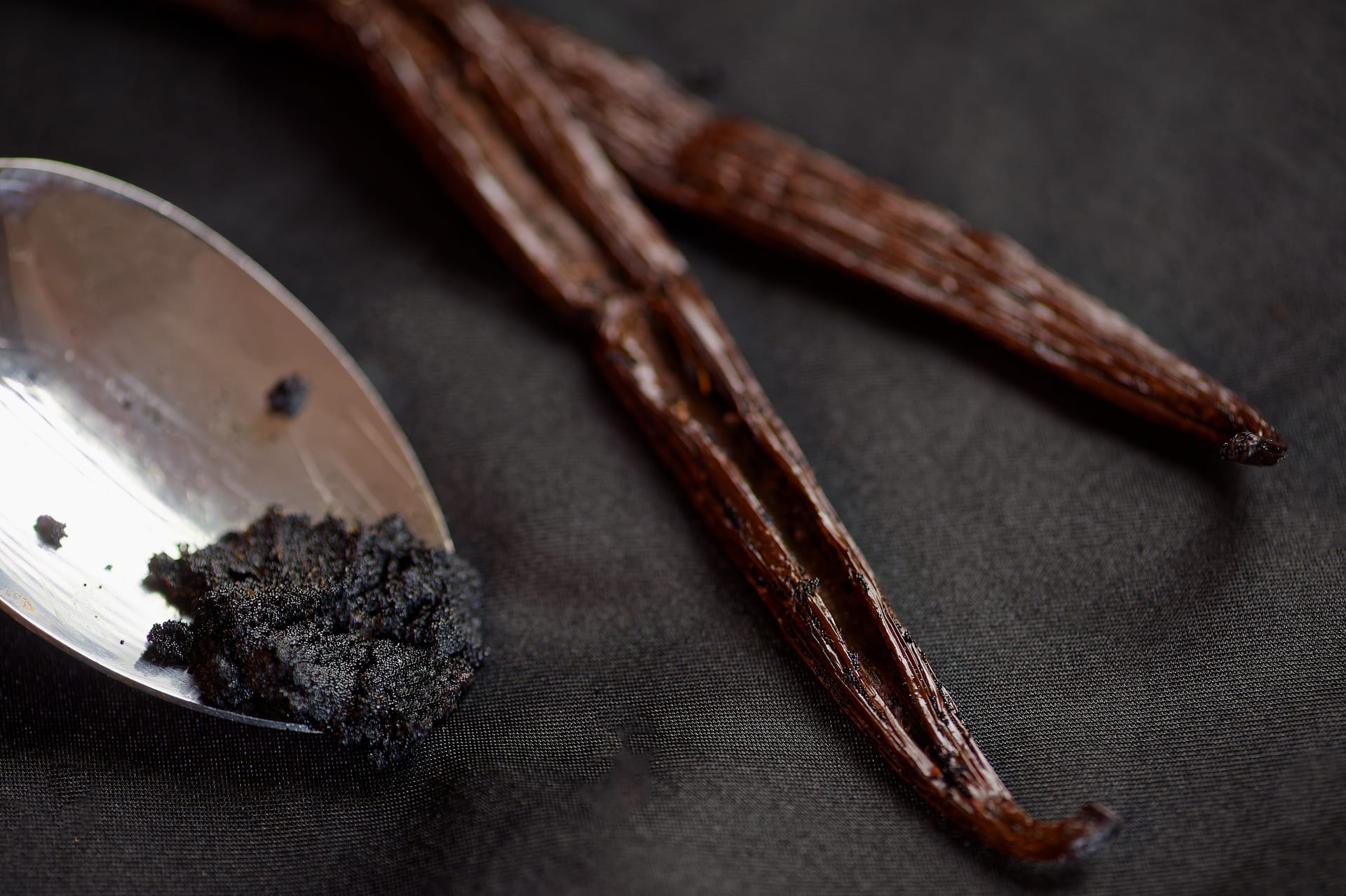 Vanilla caviar on a spoon and split pods, background texture